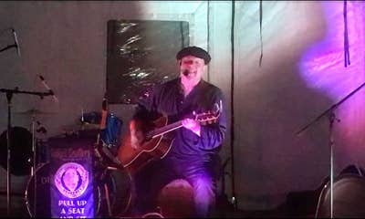 Ginger Geoffery at a festival bathed in purple light singing and lp-laying guitar