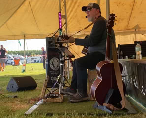 Ginger Geoffrey at Wild Festival Litchfield sat on a cajonwearing a bseball cap and sun glasses.