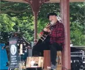 Ginger Geoffrey on a band stand in Stafford Town Park playing cajon, guitar and singing.