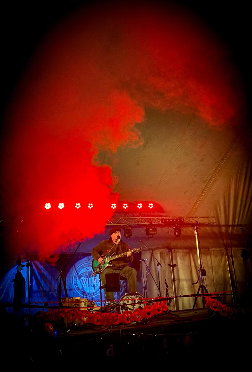 Ginger Geoffrey on stage at night surrounded by red smoke.